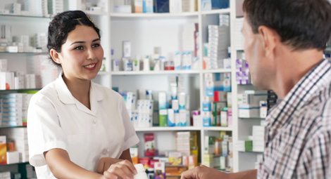A female pharmacist smiling at a customer as she passes him some medication