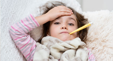 A young girl with a thermometer in her mouth and her hand held against her forehead she looks unwell