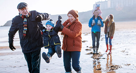 Grandparents swinging their grandchild between them while his parents carry his sibling in the background